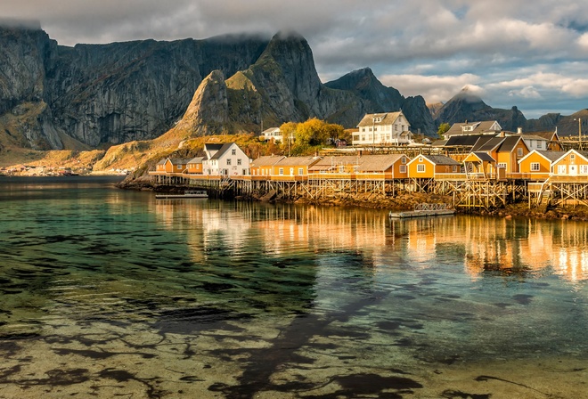 the sky, water, clouds, reflection, landscape, mountains, nature, rocks, shore, tops, the bottom, boats, Norway, houses, pond, the village, piles, The Lofoten Islands
