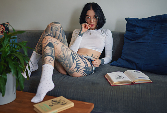 women, Sergey Fat, couch, tattoo, glasses, sitting, white socks, women indoors, books, plants, finger on lips, jean shorts, women with glasses, necklace, black hair, see-through clothing, nipples through clothing