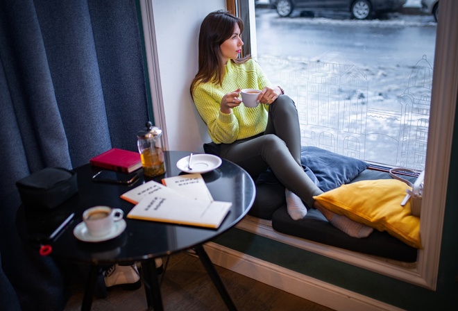 women, brunette, women indoors, model, sweater, yellow sweater, pants, black pants, window, by the window, looking at viewer, sitting, table, car, black car, coffee, looking out window