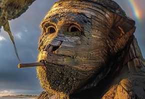 wooden sculpture, wooden gorilla, beach figure, nature art, dramatic lighting, wooden texture, shoreline, sculpture on beach, mystical sunset, sandy shore, natural art, handmade figure, vintage style, natural materials, sculpture from ship, gorilla in san