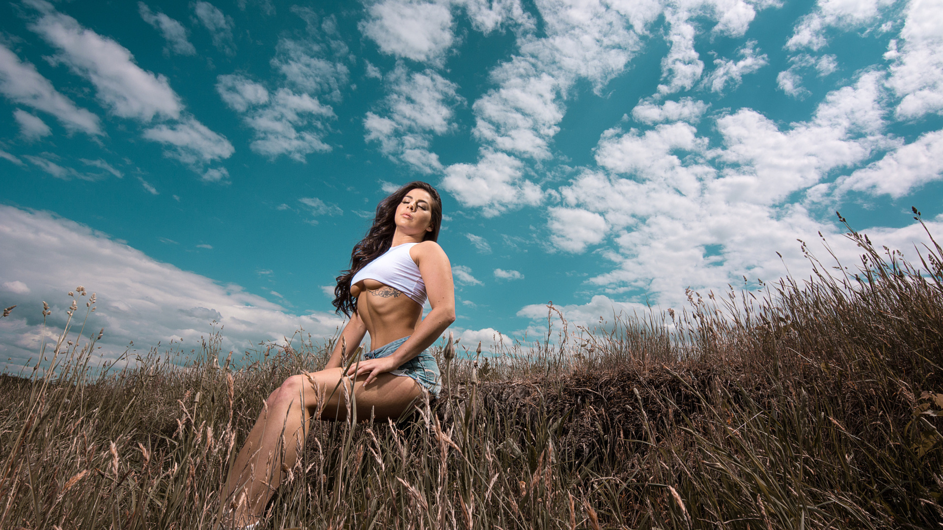 women, closed eyes, underboob, t-shirt, sitting, women outdoors, sky, clouds, tattoo, long hair, wavy hair, belly, brunette, boobs, jean shorts