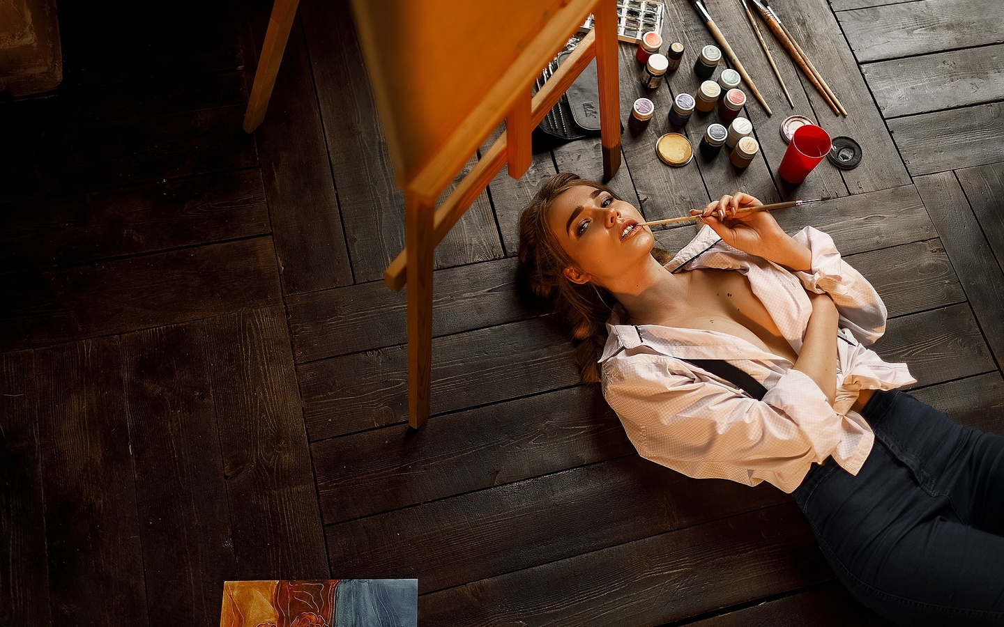 women, blonde, portrait, easel, white shirt, pants, jeans, painting, top view, lying on back, on the floor, wooden floor