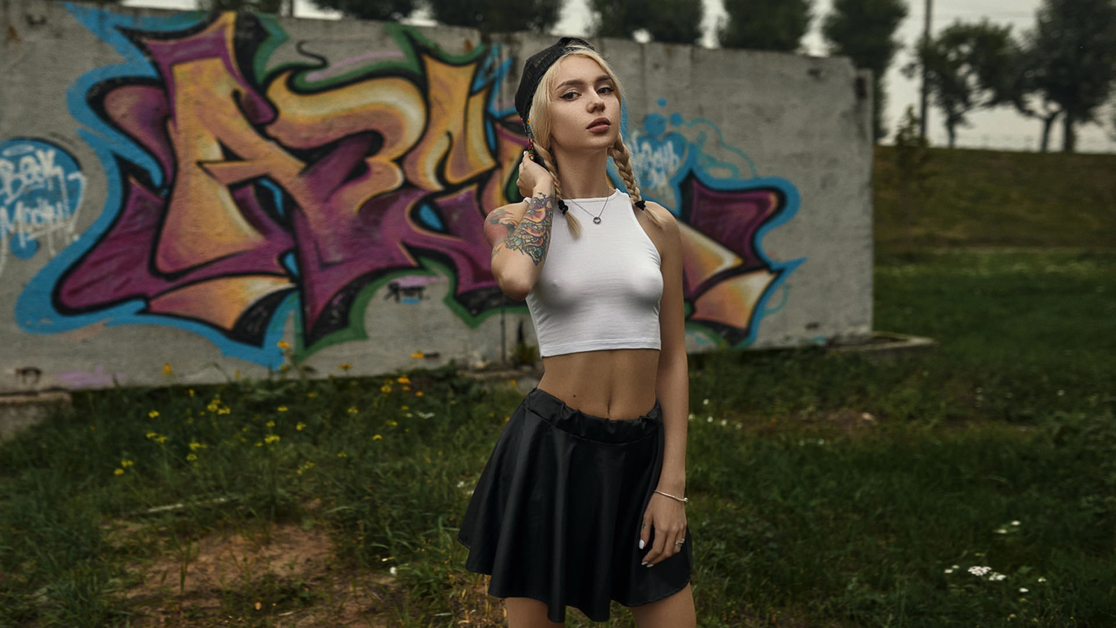 women, blonde, tank top, women outdoors, pigtails, baseball cap, wall, graffiti, grass, nipple through clothing, black skirts, tattoo, painted nails, eyeliner, belly, trees