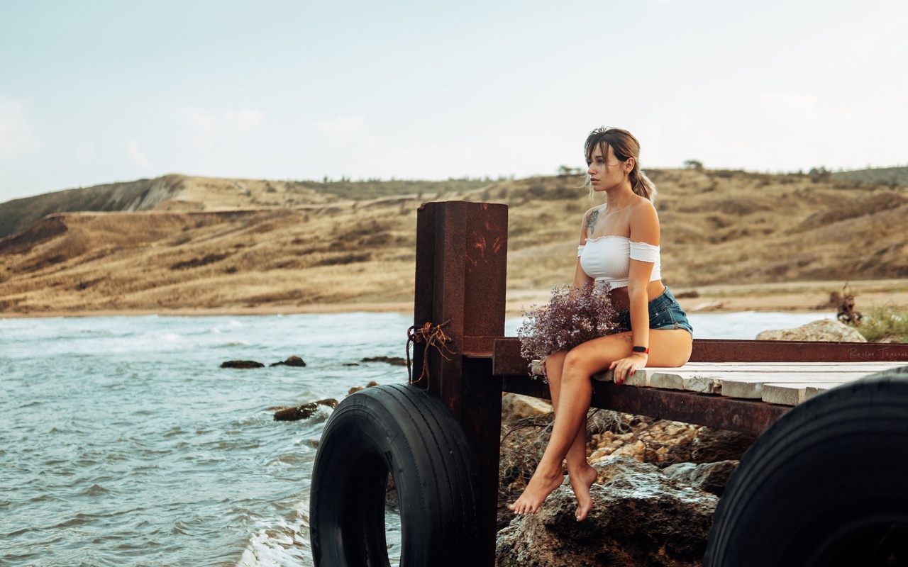 women, brunette, sea, women outdoors, jean shorts, pier, sitting, red nails, tattoo, sky, watch, tires, bare shoulders, looking away